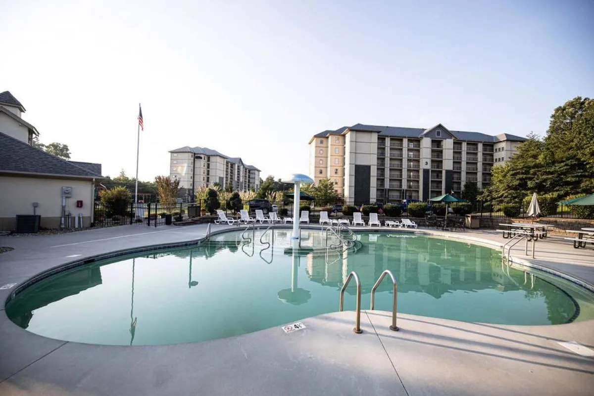 A vibrant outdoor swimming pool bordered by lounge chairs and surrounded by greenery, with the building in the background. The scene captures resort-like amenities available for relaxation and socializing after a day of exploring town.