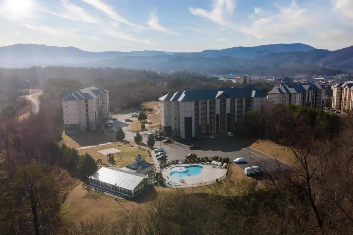 This image highlights the resort's outdoor swimming pool, set against a backdrop of the surrounding mountains and residential buildings. The pool area is open and inviting, with plenty of space for relaxation and socializing, and it captures the tranquil yet lively atmosphere of a family-friendly resort.