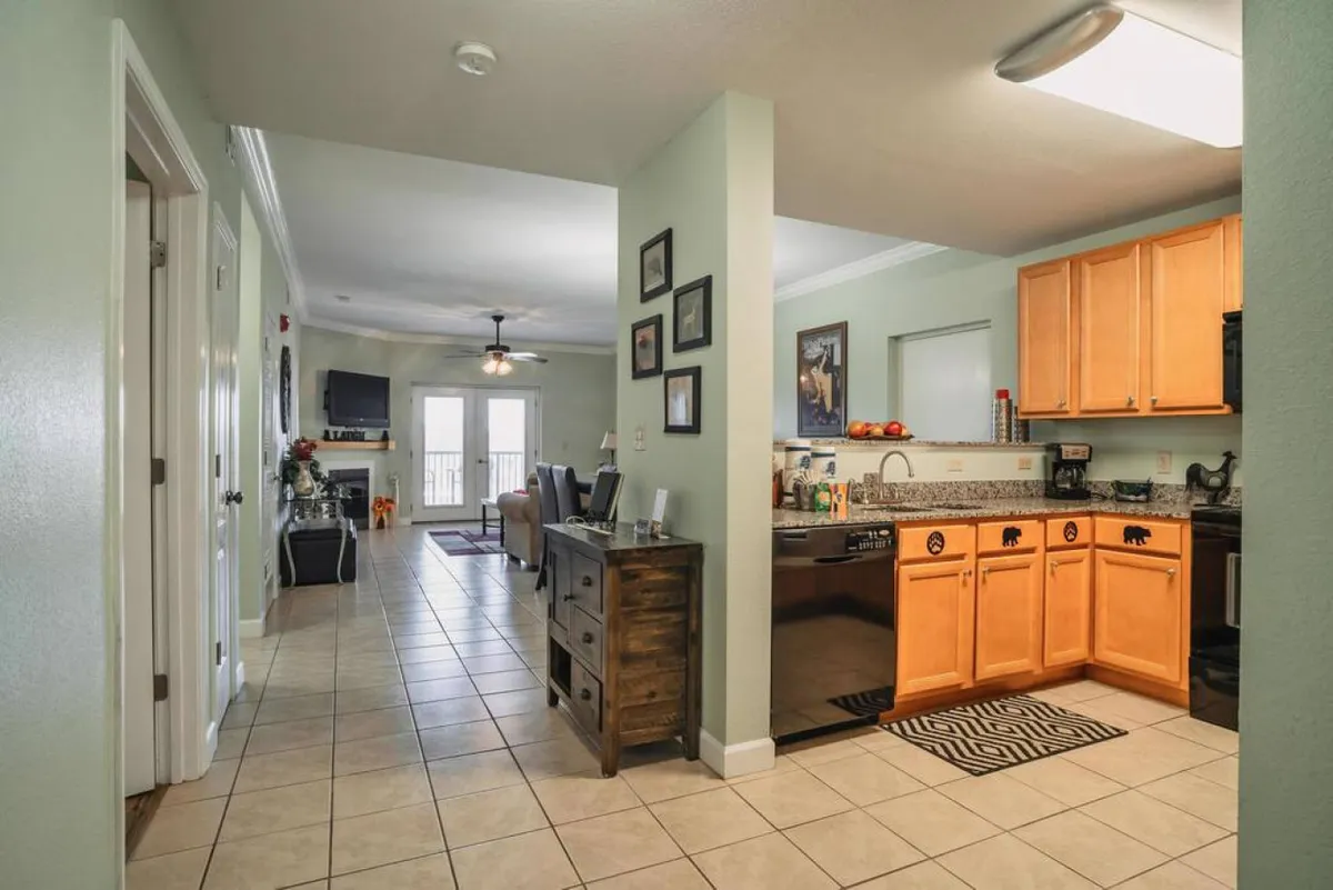 The photo provides a broader perspective of the kitchen area, leading naturally into the adjacent living room. Cabinets, wall art, and appliances are visible, suggesting an open concept layout that fosters connection between the culinary and social spaces.