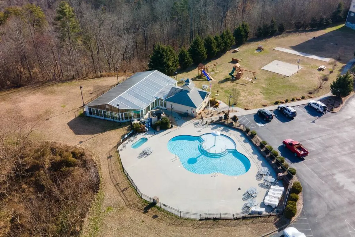 A vibrant exterior scene featuring a sun-soaked swimming pool, children playing by a whimsical mushroom fountain, a playground in the background, and gathering areas for outdoor fun and BBQs.