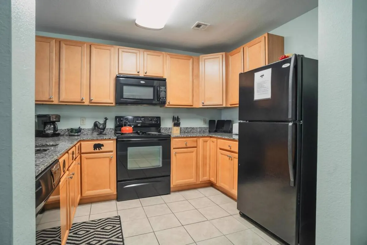 This image showcases a modern kitchen with a black refrigerator, granite countertops, and wooden cabinets. Kitchen appliances are visible, emphasizing the space's readiness for meal preparation and family cooking. The warm lighting highlights both functionality and comfort.