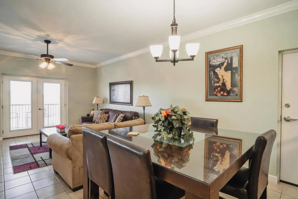 This image features an open-concept living and dining area, with a plush sofa and chairs, a dining table with chairs, striking wall art, and sliding glass doors that let in abundant natural light. The space is styled to feel welcoming and perfect for both relaxation and shared meals, with comfortable seating and an inviting atmosphere.